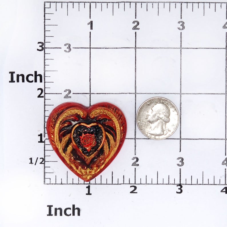 May include: A red heart-shaped resin ornament with gold and black details. The ornament features a stylised heart design with intricate patterns and a smaller heart in the centre.