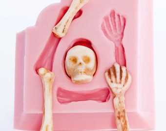 May include: Pink silicone mold with a skull and bone shapes. The mold is designed for making edible decorations for cakes or other desserts.