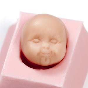 Könnte beinhalten: Eine rosa Silikonform zum Herstellen eines Baby-Puppen-Kuchentoppers. Die Form ist wie ein Babykopf geformt mit geschlossenen Augen und einem lächelnden Mund.