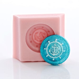 May include: A pink silicone mold with a raised design of a nautical wheel with an anchor inside. A teal blue resin casting of the design is next to the mold.