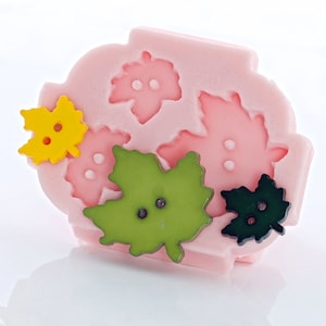 May include: A pink silicone mold with five leaf shapes. The leaves are in various colors, including yellow, green, and black. Each leaf has two small circles in the center.