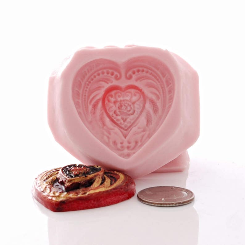 May include: Pink heart-shaped silicone mould with a detailed design of a heart with a floral pattern inside. A red heart-shaped wax seal with a similar design is shown next to the mould.