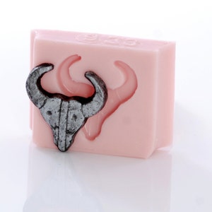 May include: A pink silicone mold with a detailed bull head design. The mold is used for making resin or polymer clay crafts.
