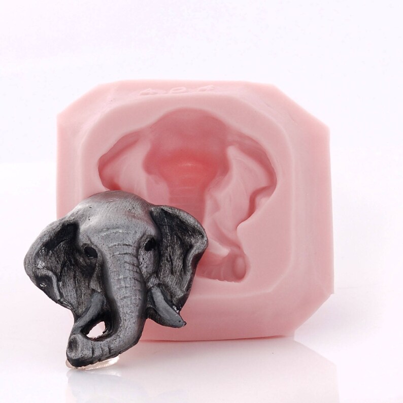 Puede incluir: Un molde de silicona rosa para hacer manualidades con forma de cabeza de elefante. Se muestra una cabeza de elefante gris junto al molde.