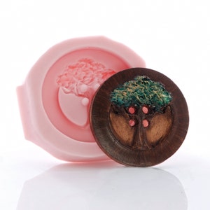 May include: A wooden button with a carved tree design. The tree has green leaves and three red apples. The button is surrounded by a dark brown ring.