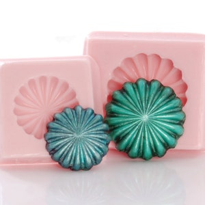 May include: Two silicone molds for making round, decorative, teal-colored resin cabochons. The molds have a scalloped design.