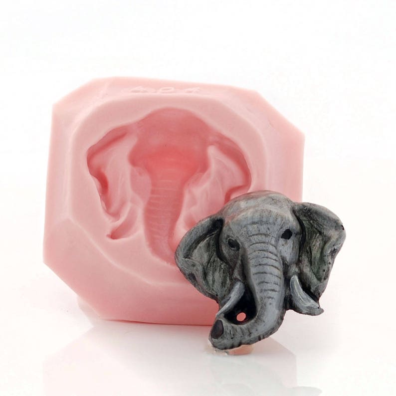Puede incluir: Un molde de silicona rosa para hacer esculturas de cabeza de elefante. El molde se muestra con una escultura de cabeza de elefante gris terminada.