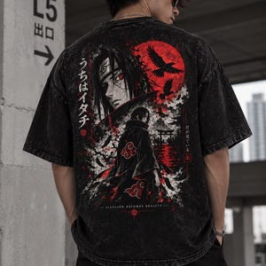 Peut inclure: Un t-shirt noir délavé à l'acide avec une impression graphique d'un personnage d'anime aux cheveux sombres et aux yeux rouges. Le motif inclut une grande lune rouge, des corbeaux en vol, du texte japonais et la phrase "ILLUSION BECOMES REALITY".