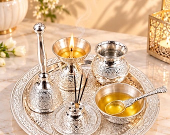 Può includere: Un set puja thali in metallo color argento composto da un vassoio circolare decorato, una campana, una lampada diya con fiamma accesa, un piccolo vaso per l'acqua, un porta incenso con tre bastoncini e una ciotola con liquido.