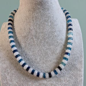May include: A beaded necklace featuring a repeating pattern of smooth, round beads in shades of translucent white, deep navy blue, and variegated light blue. The beads are uniform in size and shape, strung together to form a continuous circular strand.