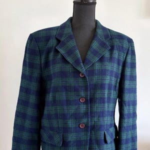 Peut inclure: Un blazer avec un motif à carreaux bleu foncé et vert forêt. Le vêtement présente un revers cranté, des manches longues et trois boutons marron foncé sur le devant. Deux poches à rabat sont situées sur le bas de la veste.