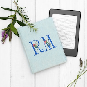 teal denim kindle case with large initials embroidered by bright blue thread, the letters have floral decoration with red flowers