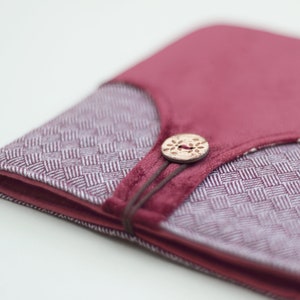 Op de afbeelding: Een close-up van een klein, bordeauxrood stoffen dagboek met een decoratieve houten knoopsluiting. Het dagboek heeft een wit en bordeauxrood ruitpatroon.
