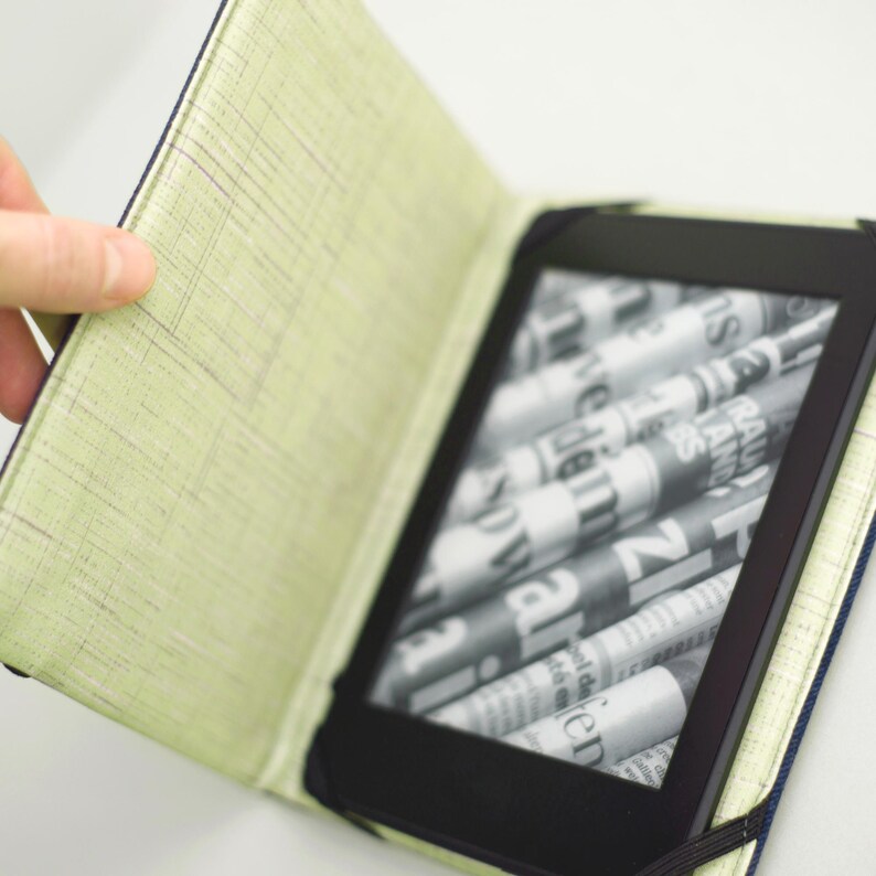 May include: A green and black e-reader case with a built-in cover. The e-reader is open and displaying a page of text.
