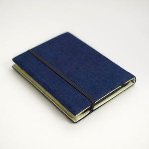 back side of kindle fabric cover made of dark blue velour with balck elastic strap as a closure, bright lining in green, thick padded e-reader case