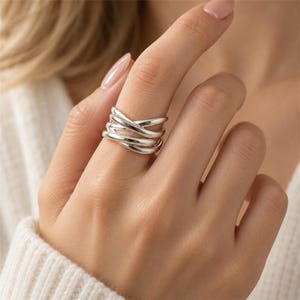 May include: A polished silver ring featuring a multi-band design with several smooth, rounded strands that cross over each other to create a layered, interconnected appearance. The metal has a reflective, high-shine finish throughout.