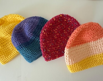 May include: Four handmade crochet beanies in a row. The beanies are in yellow, blue, red, and orange. The yellow beanie has a textured stitch. The blue beanie fades from blue to teal. The red beanie has flecks of color. The orange beanie has stripes.