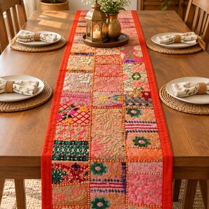 Handmade patchwork table runner featuring colorful embroidered and beaded Indian fabric pieces, intricate floral and paisley patterns, vibrant textile details, and a decorative border.