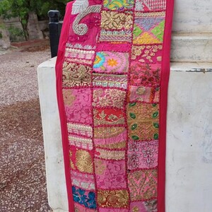 Handmade patchwork table runner featuring colorful embroidered and beaded Indian fabric pieces, intricate floral and paisley patterns, vibrant textile details, and a decorative border.