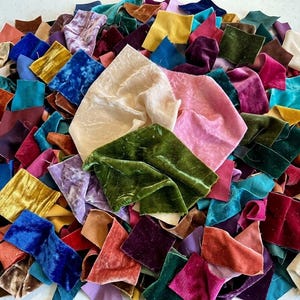 Könnte beinhalten: Eine große Sammlung kleiner, quadratischer Samtstoffreste in einer Vielzahl von Farben, darunter Creme, Rosa, Olivgrün, Senfgelb, Königsblau, Blaugrün, Burgunderrot und Violett, die in einer dichten, überlappenden Anordnung gestapelt sind.