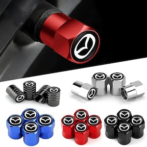 May include: A collection of cylindrical tyre valve stem caps featuring the Mazda logo on the top. The set includes multiple colour options such as metallic red, blue, black, and silver, each with a hexagonal base and a threaded interior design.