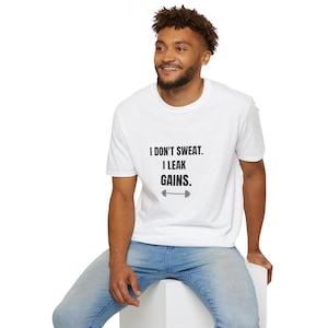 May include: A white short-sleeved t-shirt featuring the black printed text I DON'T SWEAT. I LEAK GAINS. accompanied by a small black barbell icon centered on the chest. The garment has a classic crew neckline and a standard fit design.