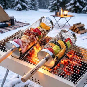 Könnte beinhalten: Zwei zylindrische Grillkörbe aus Edelstahl-Drahtgeflecht mit hellen Holzgriffen, einer davon mit dem eingravierten Namen Oliver, gefüllt mit Gemüse und Fleisch, platziert über einem Holzkohlegrill mit glühender Kohle.