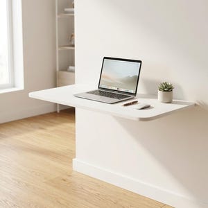 May include: A white wall-mounted floating desk featuring a silver laptop, a dark pen, a white computer mouse, and a small green succulent in a light gray pot. The desk has a smooth, rectangular surface with rounded corners.