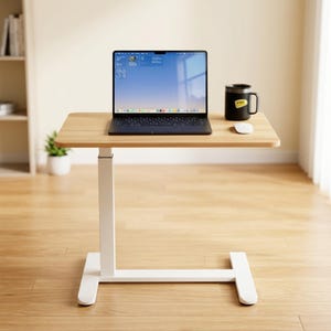 May include: A height-adjustable desk with a light wood-grain rectangular top and a white metal base. A dark gray laptop is open on the desk surface next to a black mug with a yellow label and a white computer mouse.