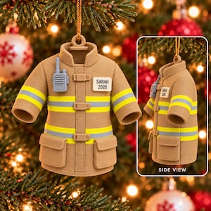 May include: A tan firefighter turnout coat ornament featuring yellow and grey reflective stripes, two front pockets, a grey radio on the chest, and a white name tag printed with the text SARAH 2026. The ornament includes a gold hanging string.