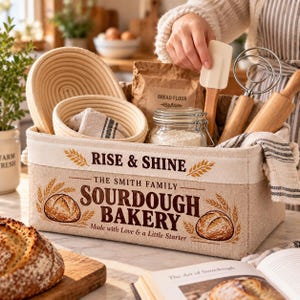 以下が含まれることがあります： RISE & SHINE THE SMITH FAMILY SOURDOUGH BAKERY MADE WITH LOVE & A LITTLE STARTERとプリントされた長方形のベージュの布製収納バスケット。バスケットには、2つの丸い籐製の発酵かご、ガラス瓶、木製の調理器具が入っています。