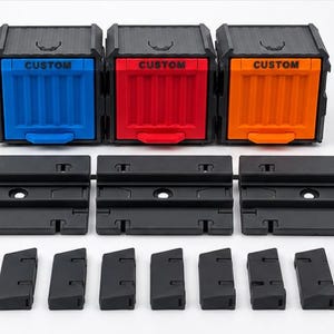 May include: Three modular storage cubes with black frames and blue, red, and orange drawers, each labeled with the word CUSTOM. The set includes three black rectangular mounting plates and nine small black rectangular connector pieces for assembly.