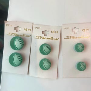 May include: Three sets of two round, mint green buttons on white display cards labeled Streamline. Each card features a unique model number: K7211, K7210, and K7209. The buttons have a textured, ribbed design with a smooth, circular center section.