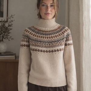 Pode incluir: Uma camisola de malha bege com gola alta e mangas compridas. A parte superior do peito e os ombros são decorados com um padrão circular em tons de castanho, cinzento e creme, com punhos e bainha canelados.