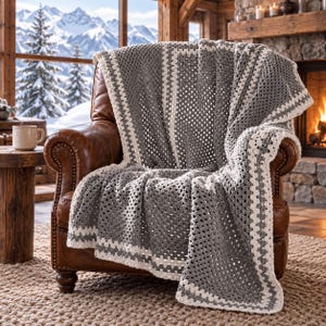 May include: A crochet blanket featuring a repeating granny square pattern in alternating blocks of dark gray and cream white yarn, draped over a brown leather armchair with visible nailhead trim along the front armrests.