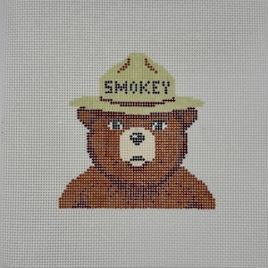 May include: A needlepoint canvas featuring a brown bear wearing a light tan ranger hat with the word SMOKEY stitched in black across the front. The bear has a cream-colored muzzle, dark brown fur, and is centered on a white grid mesh background.