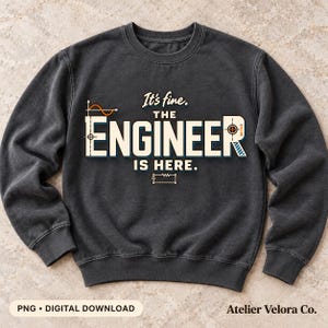 Op de afbeelding: Een antracietkleurige sweater met ronde hals en de tekst It's fine. THE ENGINEER IS HERE. in witte en crèmekleurige letters. Het ontwerp bevat oranje en blauwe technische ingenieursymbolen zoals een sinusgolf en een weerstand.