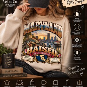 Puede incluir: Una sudadera de cuello redondo en color beige con un estampado gráfico que incluye el texto MARYLAND RAISED OLD LINE STATE SOUL. El diseño muestra un cangrejo azul sobre un poste de madera, un horizonte urbano al atardecer y un faro.
