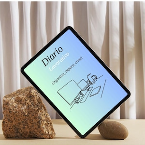 Puede incluir: Una tableta digital que muestra una pantalla con degradado azul y verde con el texto Diario Lavorativo y Organizza, impara, cresci, con una ilustración de línea de un escritorio, colocada entre dos rocas naturales de color marrón.
