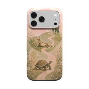 May include: A smartphone case featuring a soft-toned illustration of a hare resting on a grassy hill above a walking tortoise, both positioned along a winding pink path surrounded by flowers, trees, and a crescent moon under a pale sky.
