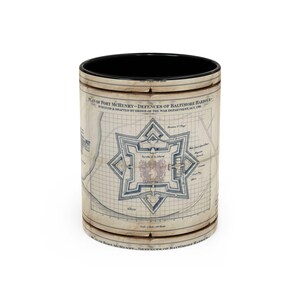 May include: A cylindrical mug with a black interior and a beige exterior featuring a historical map titled Plan of Fort McHenry - Defences of Baltimore Harbour, surveyed and drafted by order of the War Department, Oct 1799, with blue ink lines.