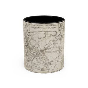 May include: A cylindrical mug with a black interior and a cream-colored exterior featuring a historical map titled Plan of the Operations of General Washington against the Kings Troops in New Jersey from December 1776 to January 1777 by William Faden.