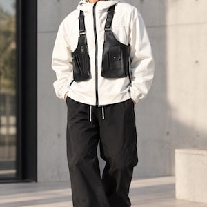 Könnte beinhalten: Eine schwarze Baseballkappe mit weißem Text, eine weiße Kapuzenjacke mit schwarzem Reißverschluss, ein schwarzes Brustgeschirr mit zwei Taschen und Riemen, eine schwarze Hose mit Kordelzug und weiße Sneaker. Das Logo ELEGANT THREADS HEART ist sichtbar.