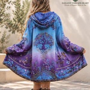 Puede incluir: Una chaqueta con capucha en degradado azul y morado, con un gráfico central de un árbol y motivos florales. En la parte posterior aparece el texto ELEGANT THREADS HEART Threads of Elegance, Made for You. La prenda tiene mangas largas y dobladillo.