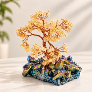 May include: A decorative tree sculpture featuring yellow citrine crystal chips as leaves attached to twisted copper wire branches. The tree is anchored to a base composed of iridescent blue and purple titanium-coated quartz crystal points.