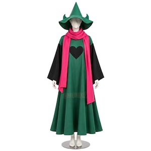 Puede incluir: Un vestido largo de color verde con mangas largas negras y un gráfico de corazón negro en el pecho. El conjunto incluye un sombrero puntiagudo verde a juego con detalles laterales curvos y una bufanda larga de color rosa sólido.