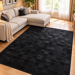 Puede incluir: Una alfombra rectangular con un diseño de patchwork compuesto por numerosas piezas cuadradas pequeñas de cuero negro. La alfombra está colocada sobre un suelo de madera clara, cubriendo gran parte de la superficie visible.
