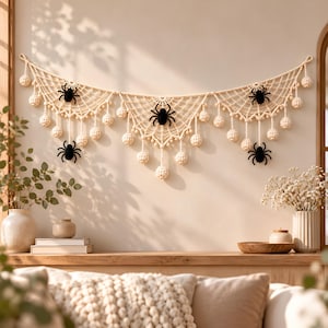 May include: A cream-colored crocheted wall hanging featuring a spiderweb pattern, adorned with multiple small hanging spheres and four black spiders attached to the web. The piece is suspended by a cord and spans horizontally across the wall.