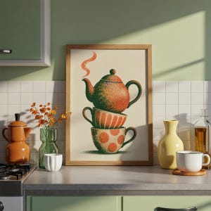 May include: A framed wall art print featuring a vertical stack of a speckled orange teapot and two patterned teacups. The teapot has a small orange steam wisp. The middle cup has orange stripes, and the bottom cup has orange polka dots.