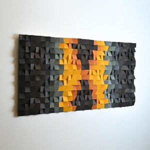 May include: A rectangular wall art piece composed of numerous small, individual wooden blocks arranged in a mosaic pattern. The blocks feature varying depths and are stained in shades of charcoal black, dark gray, and a vibrant, central vertical stripe of orange.